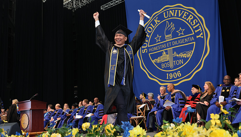 A triumphant graduate of the Sawyer Business School raises his hands as he crosses the stage at Commencement 2023.