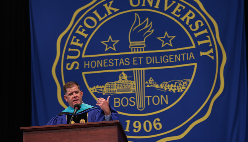 CAS Commencement speaker Martin J. Walsh speaks at a podium during the Commencement exercises in front of the Suffolk University seal