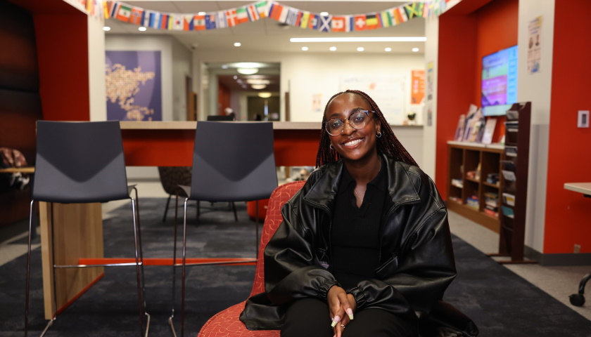 Stephanie Bulega-Nasuna smiles as she sits in front of a string of international flags on campus