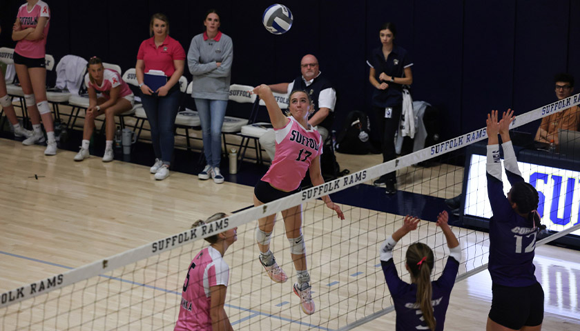 McKenna Keowen spikes the volleyball over the net while other players and coaches look on