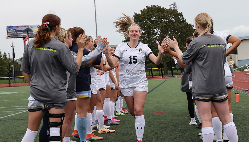 Soccer player Alyssa Belmont smiles as she runs between her teammates, who give her high-fives as she goes by