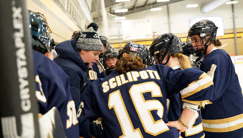 The Suffolk Women's Hockey Team gather at the boards to talk with Coach Taylor Wasylk