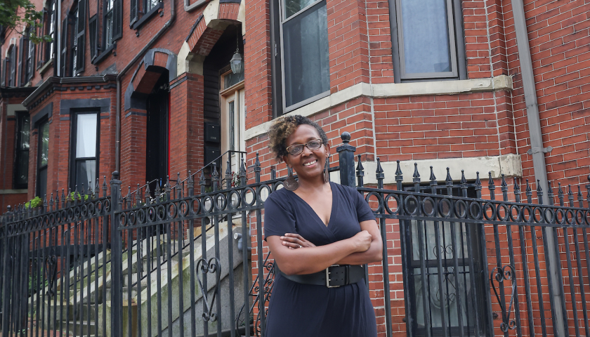 Marjorie Salvodon stands with arms crossed in front of the brick building, the former home of Suffolk founder Gleason Archer