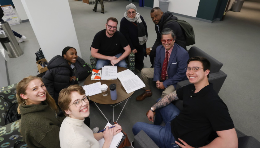 Rodrigues and seven of his international relations students smile and face the camera as their sit in a circle outside of their classroom