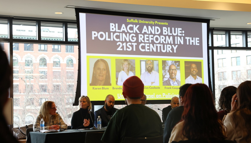 Panelists sit at a table in front of a screen reading "Black and Blue: Policing Reform in the 21st Century"