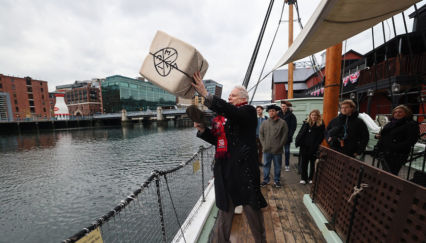 Professor Bob Allison heaves a crate of tea into Boston Harbor