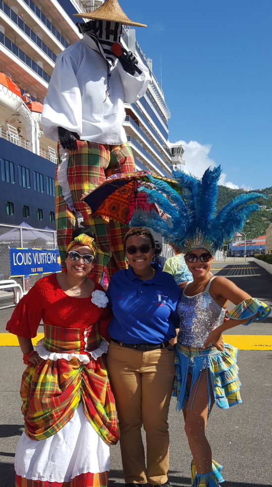 Rae'Niqua poses with two tourism workers in vivid costumes in front of a stilt walker