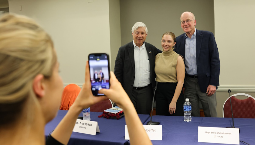An attendee takes a photo with her phone of Former US Representatives Fred Upton and Joe Hoeffel with another attendee at a Suffolk panel