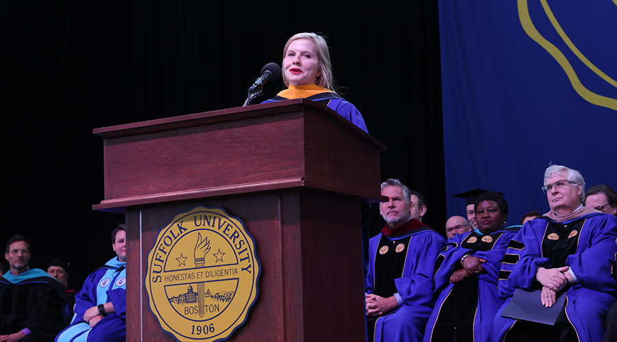 Frida Polli wears academic regalia as she stands at a podium during her keynote speech on stage at the leader bank pavilion