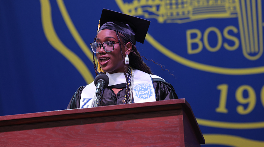 Areta Odiah in academic regalia speaks at the podium on stage at the leader bank pavilion