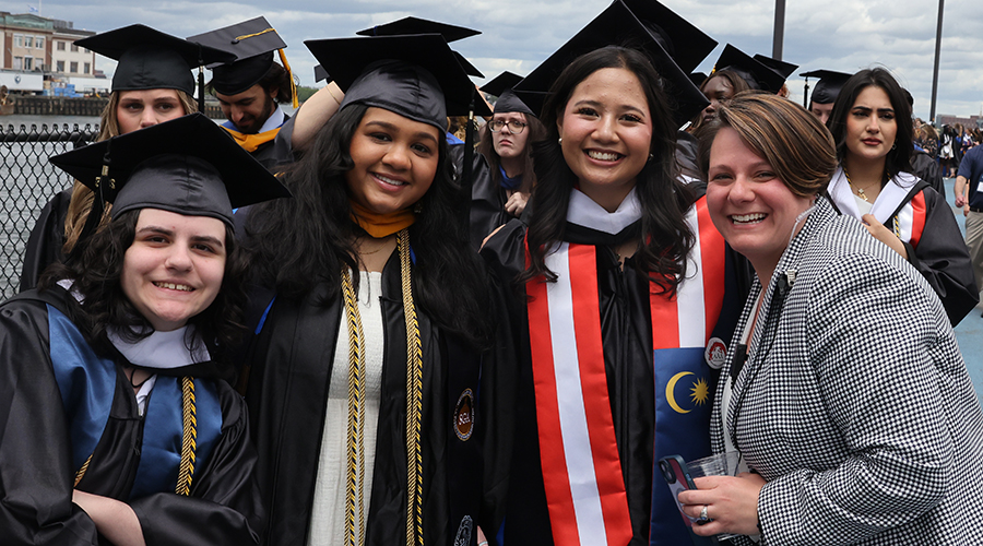 Three students in caps and gowns and an administrator outside the 2025 College of Arts & Sciences Commencement