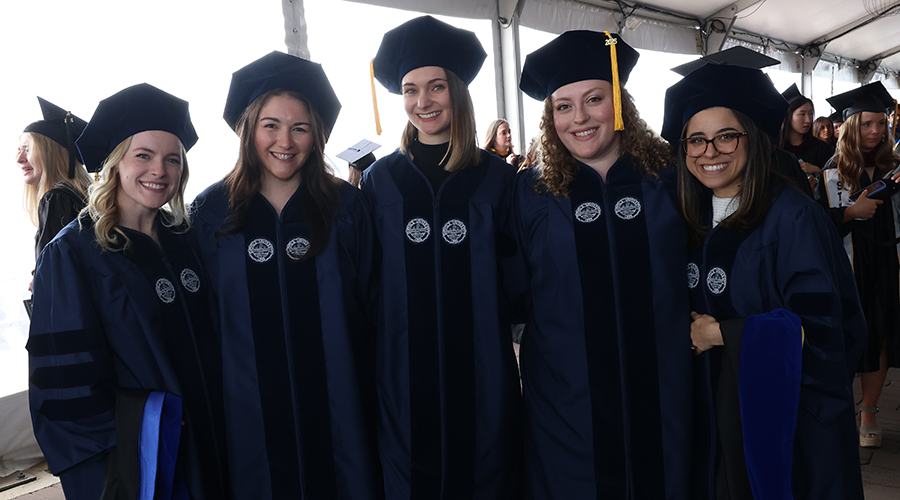A group of five PhD candidates wearing tams and gowns