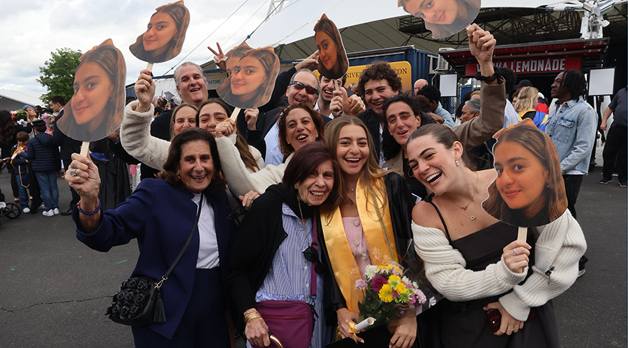 A family celebrating their student's graduation holding up cut-outs of her face