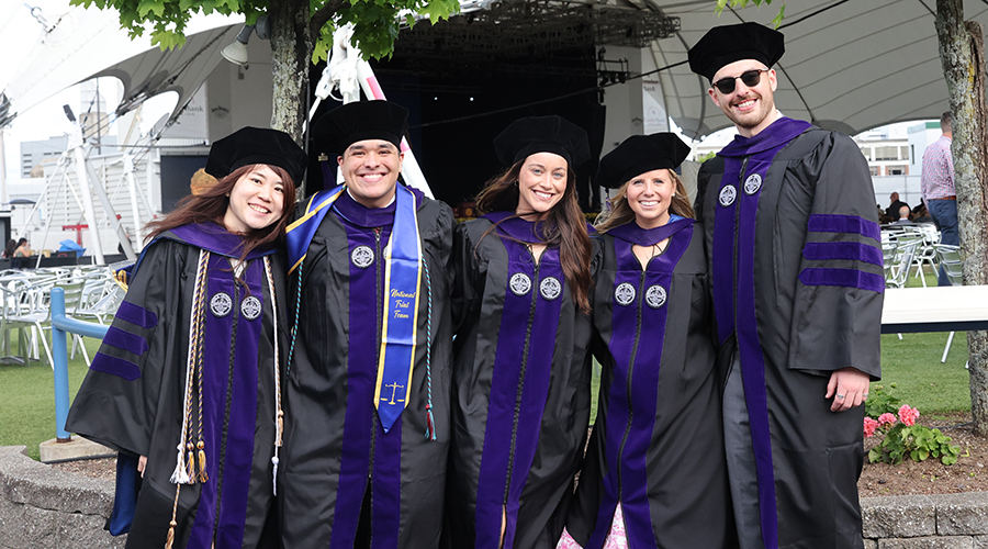 Five graduates in their tams and gowns with purple stoles at the 2025 Suffolk Law School Commencement