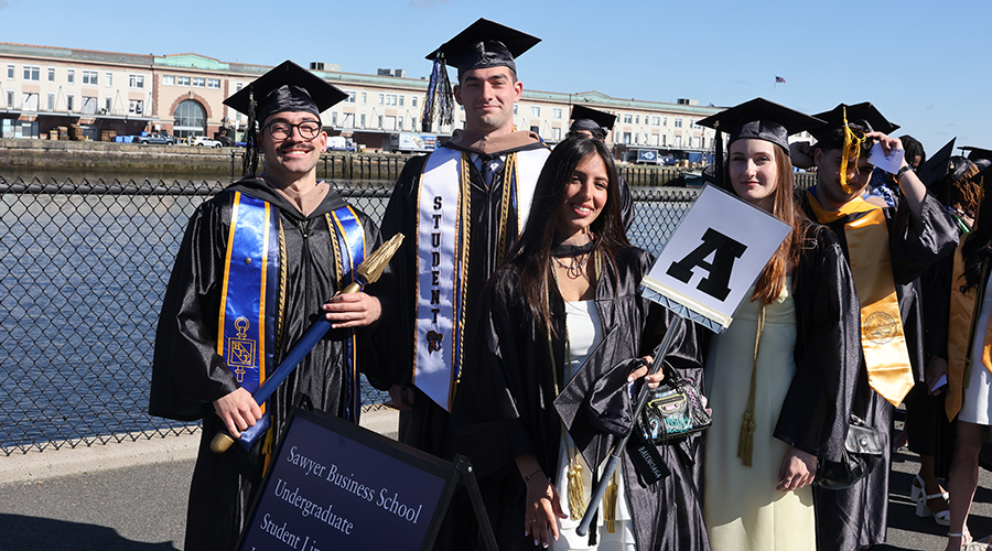 Graduating students smile in their regalia outside the Leader Bank Pavilion as they line up