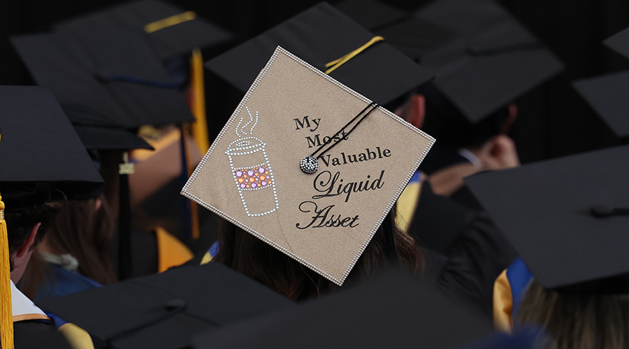 mortar board at Commencement 2025 reads "most valuable liquid asset" with drawing of a coffee cup