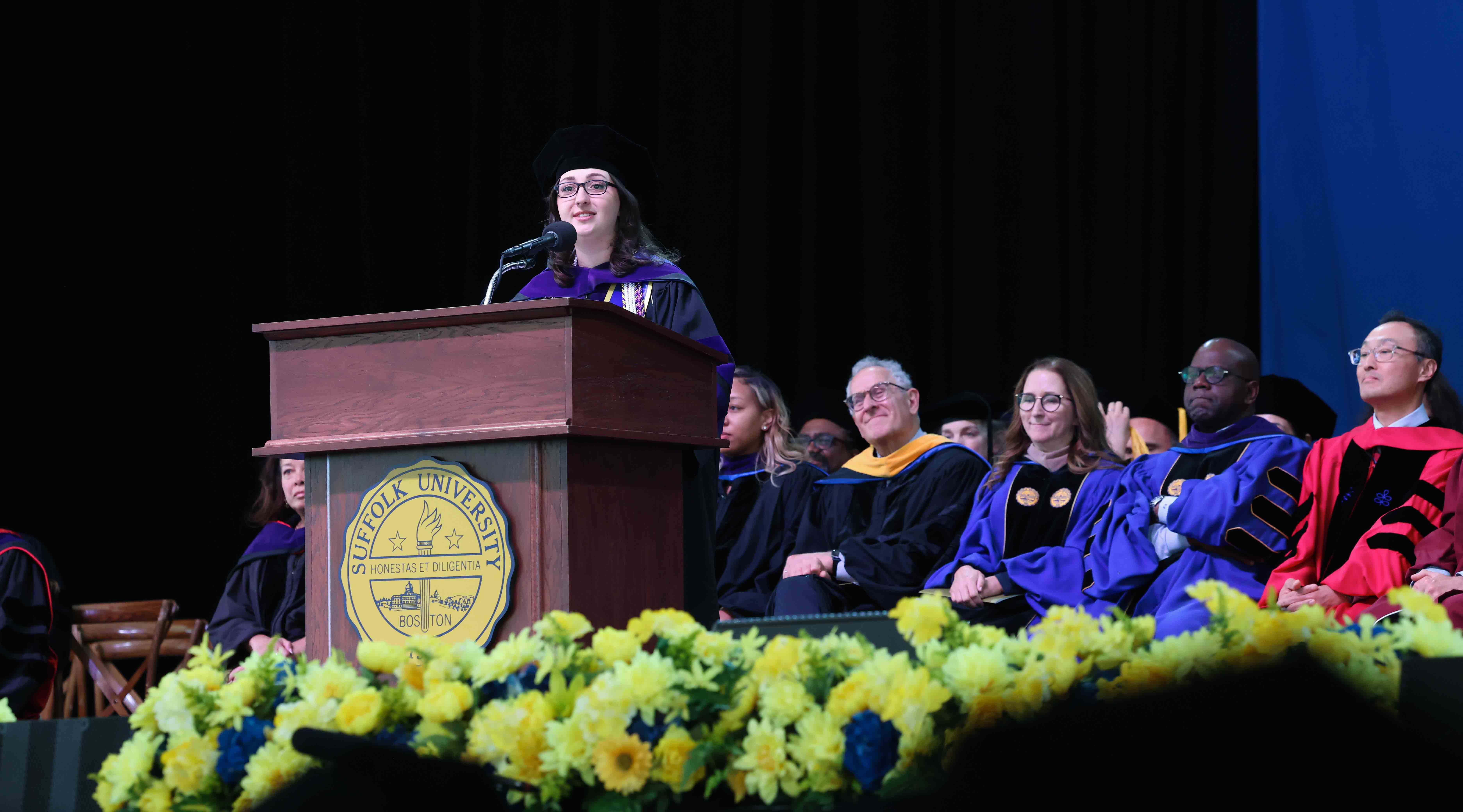 A woman named Lauren Martins speaking on the stage at the podium during the 2025 Suffolk Law Commcencement