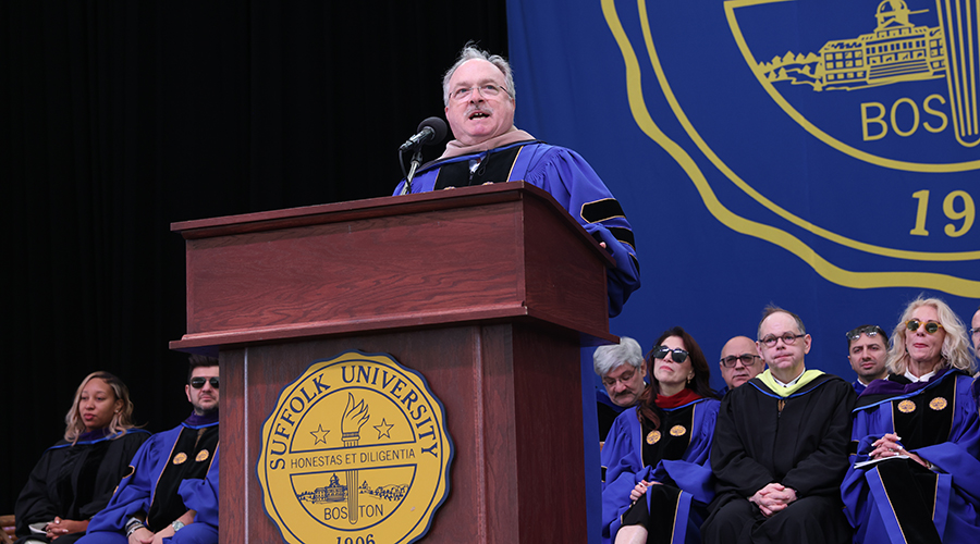 A man named Fernandez on stage speaking from the podium on stage at the 2025 Sawyer Business School Commencement