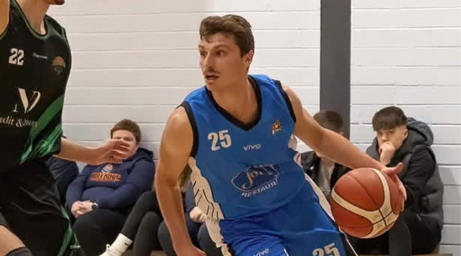 A Suffolk men's basketball player dribbling the ball, trying to get round a defender
