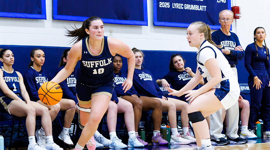 A woman basketball player on the court making a drive to the hoop with the ball and being watched by an opposing player