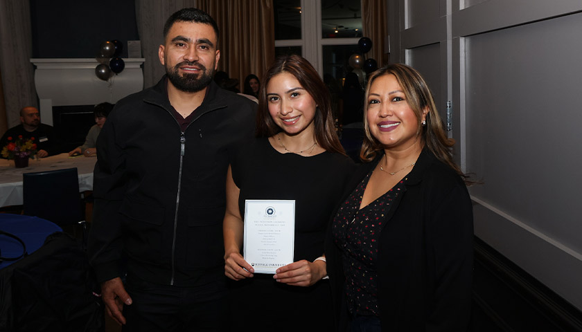 A first-gen Suffolk student celebrates her induction into the Tri-Alpha Honor Society with her parents