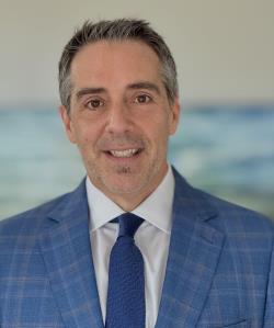 Headshot of Sean Riley in a blue plaid suit jacket and dark blue tie
