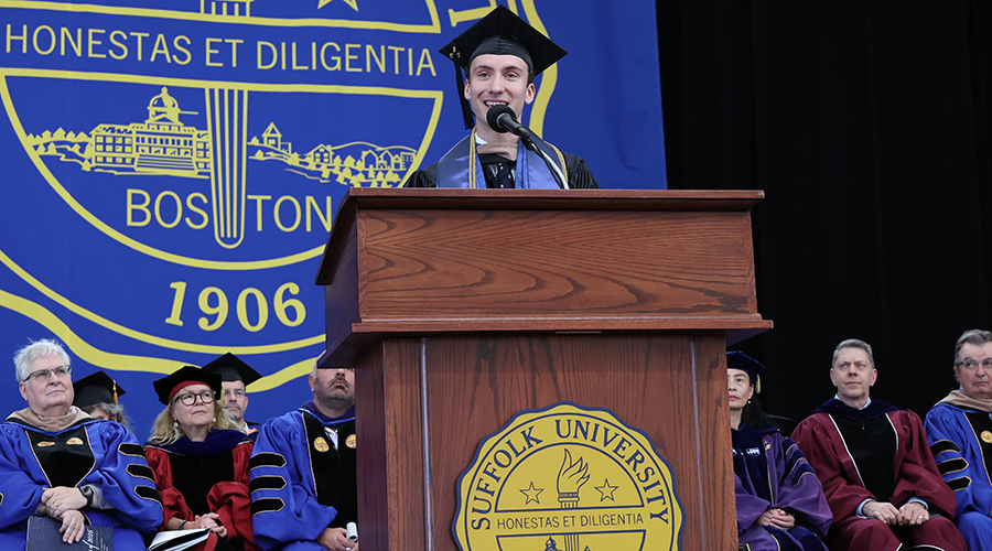 Standing at the podium with the Suffolk seal behind him, Michael Oliveri addresses the graduates of the Class of 2026