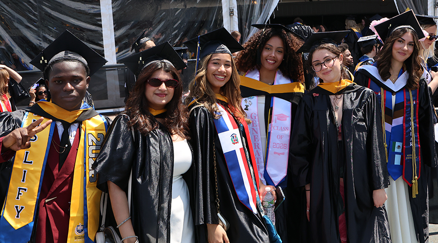 Wearing caps, gowns, and fancy stoles, a group of graduates waits to head in to Commencement ceremonies for Suffolk University's College of Arts & Sciences.