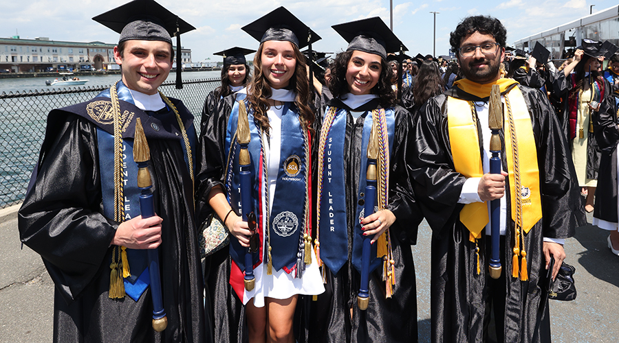 Student marshals in caps and gowns with colorful stoles waiting at the seaport for Commencement to start