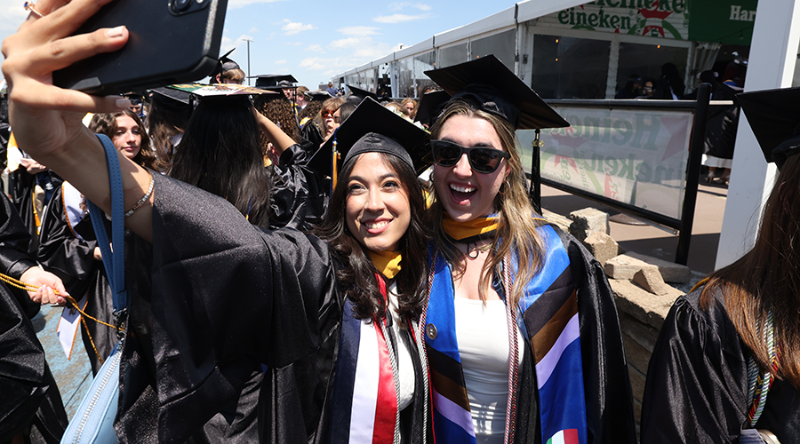 Two students in caps and gowns take a selfie ahead of the College of Arts & Sciences Commencement 2026