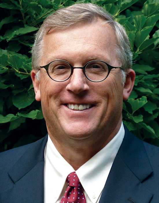 Trustee Robert Lamb smiles while standing in front of greenery
