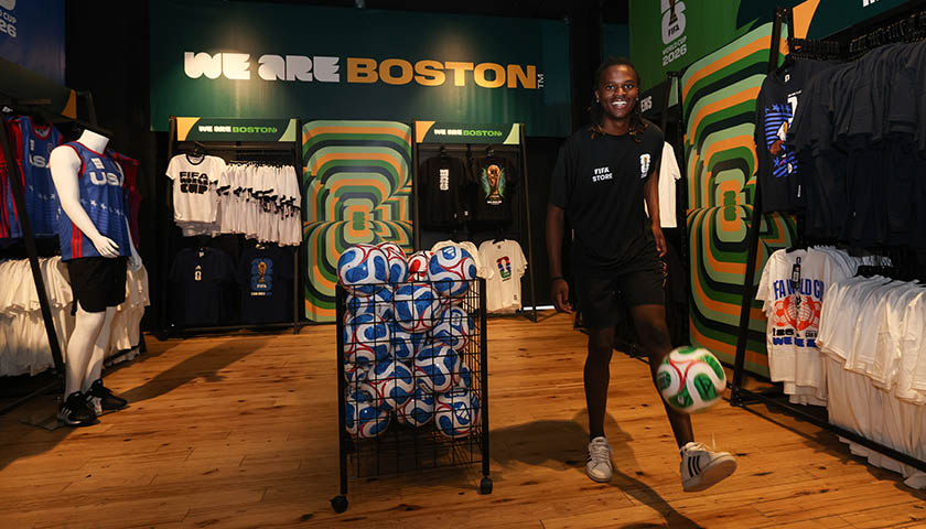 Suffolk student retail associate Tinashe Muhlauri kicks a FIFA World Cup ball surrounded by racks of official merchandise