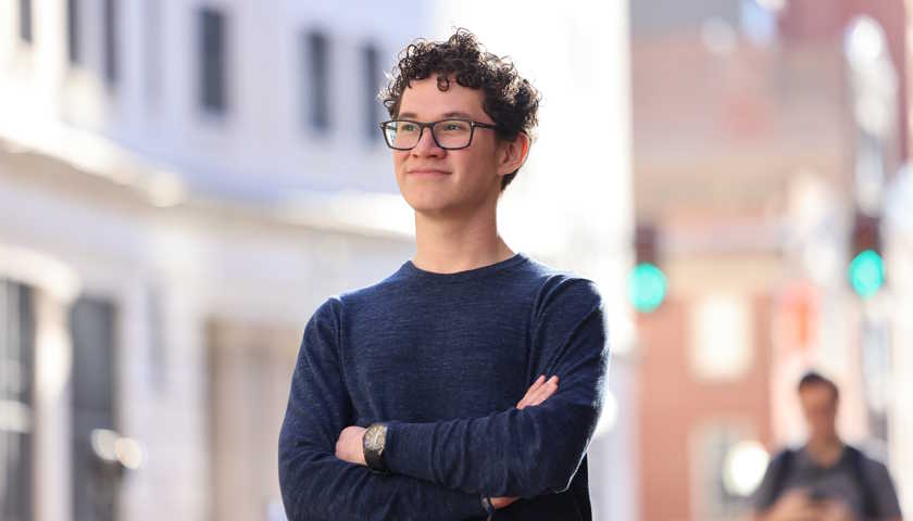 A student with glasses and a blue sweater looks into the distance outside Suffolk on Tremont Street with arms crossed.