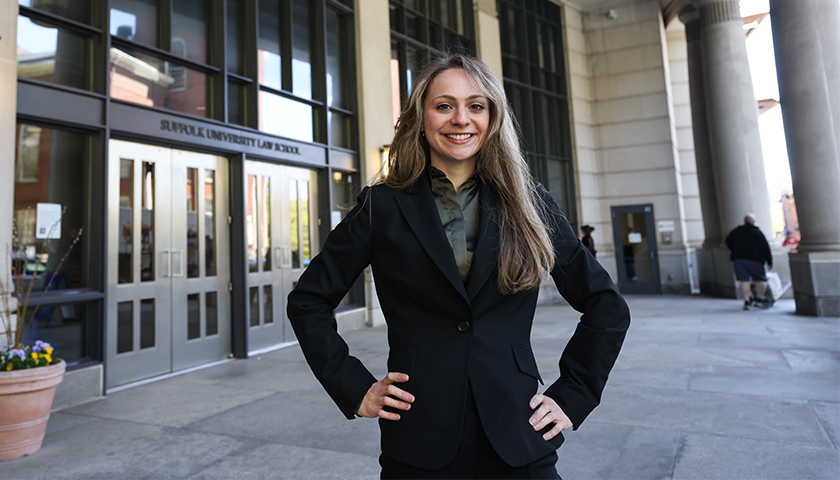Hannah Hubler in a dark suit blazer stands confidently at the front door of Suffolk Law