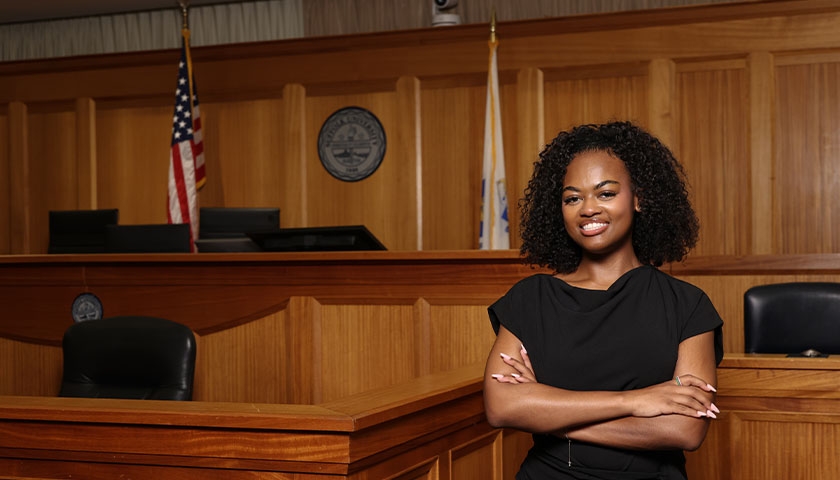Law student Jordan Moore stands with her arms crossed in Suffolk Law’s mock courtroom