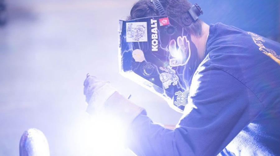Moody image of Marcus Frem wearing a welding mask and using an arc welder