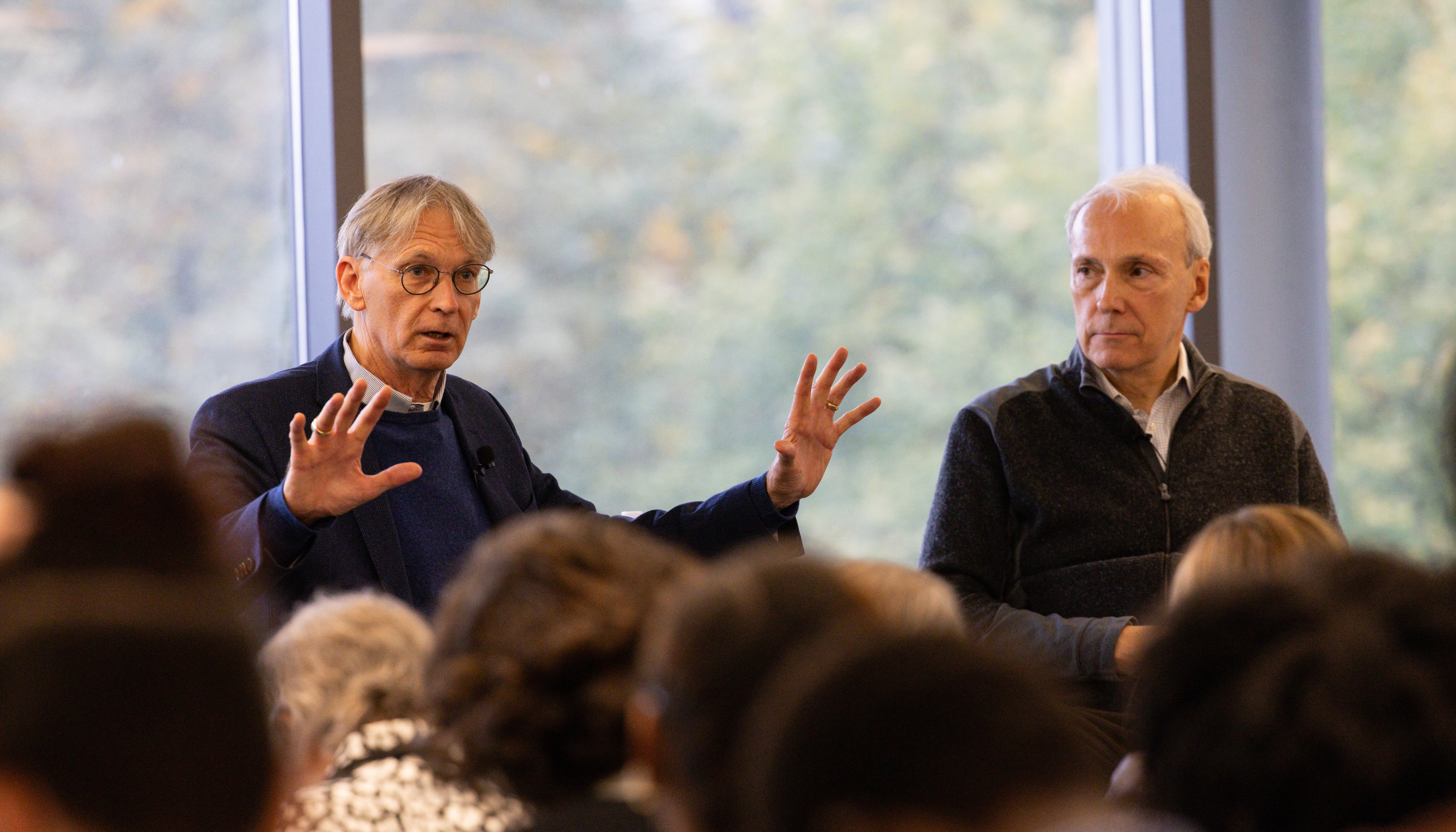 Timothy Ryback and Tim Phillips sit in front of a crowd in Smith Commons, with Ryback speaking and gesturing