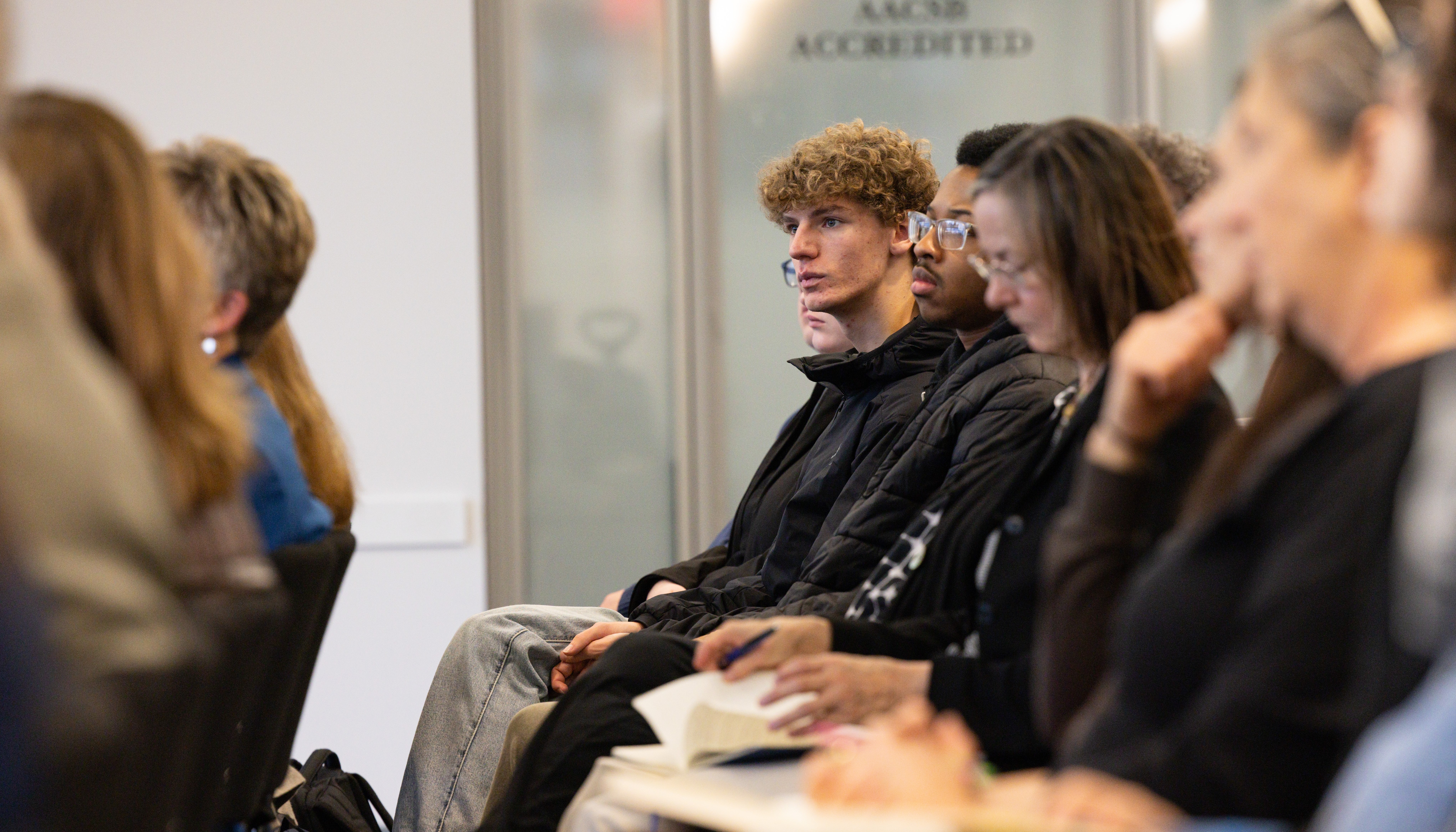 A row of people seated in the audience, focusing on a male student