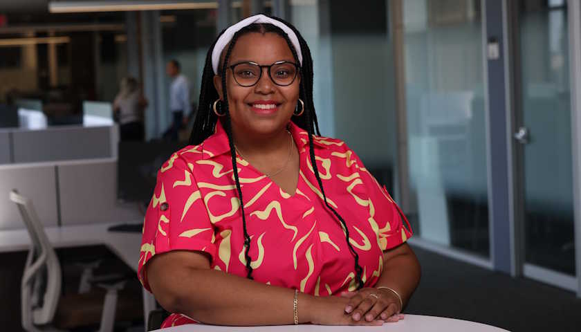 Rae'Niqua Victorine smiles as she stands, arms folded at a table, on the Suffolk campus