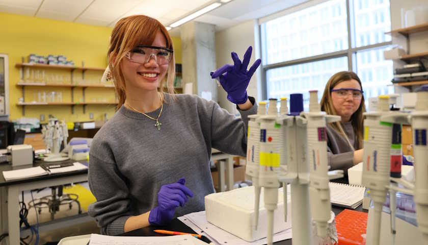 Student in safety goggles smiles at her lab bench