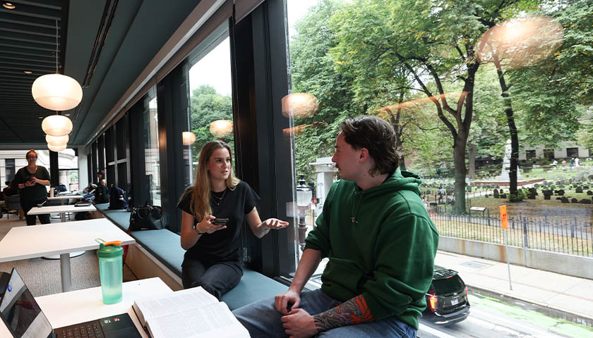 Two students seated in front of the lounge’s large picture windows overlooking the Granary Burying Ground