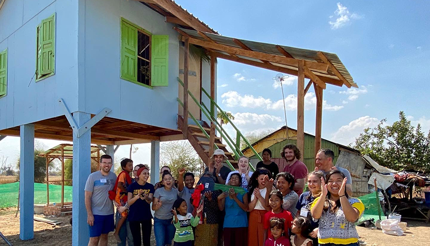 Cambodian family and students in front of house on stilts