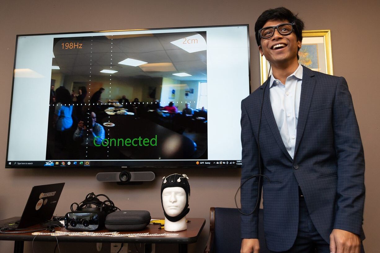 A student stands in the X-Lab in front of a display screen