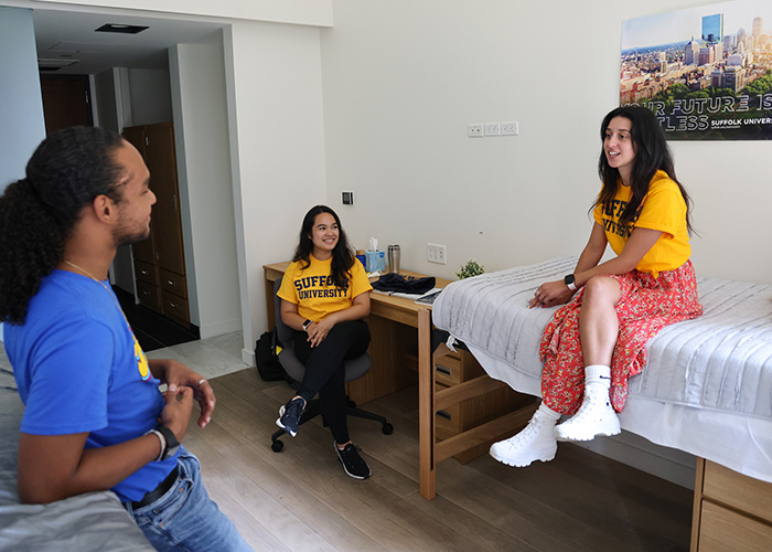Three Suffolk students sit together in a dorm room chatting
