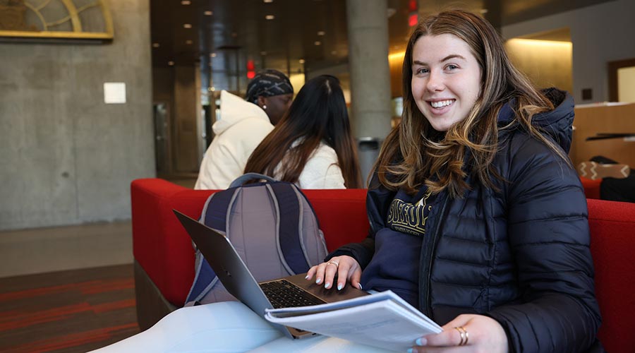 A Suffolk student sits in an on-campus lounge space with a laptop and a notebook.