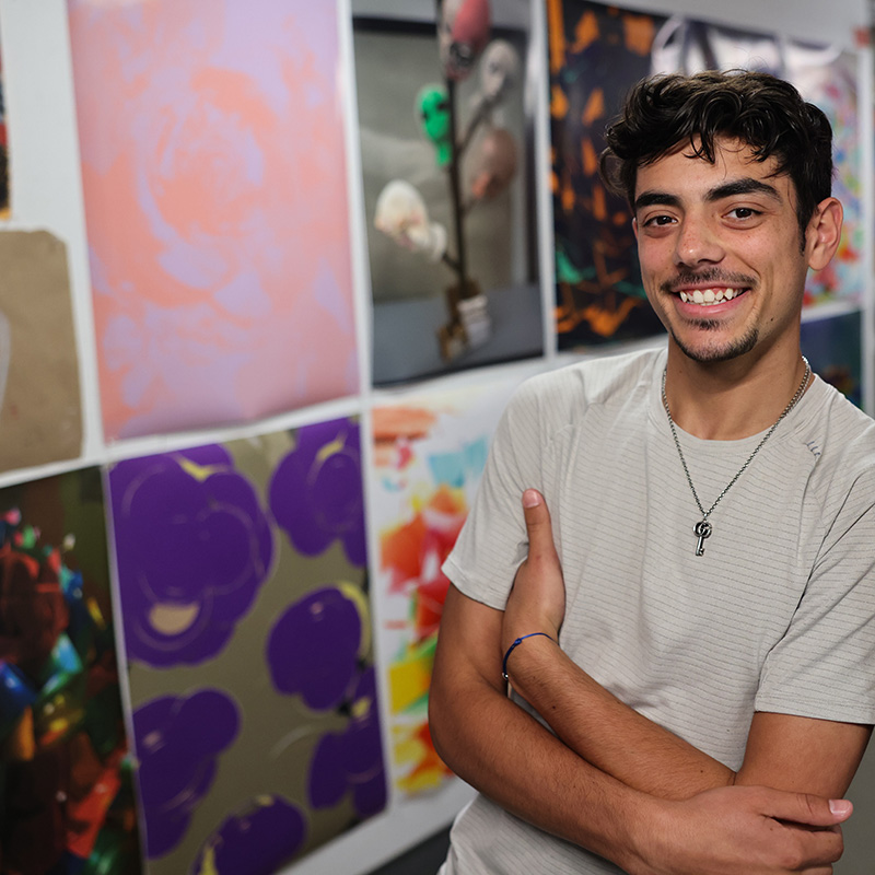 An art student leans on a gallery wall, surrounded by colorful artwork