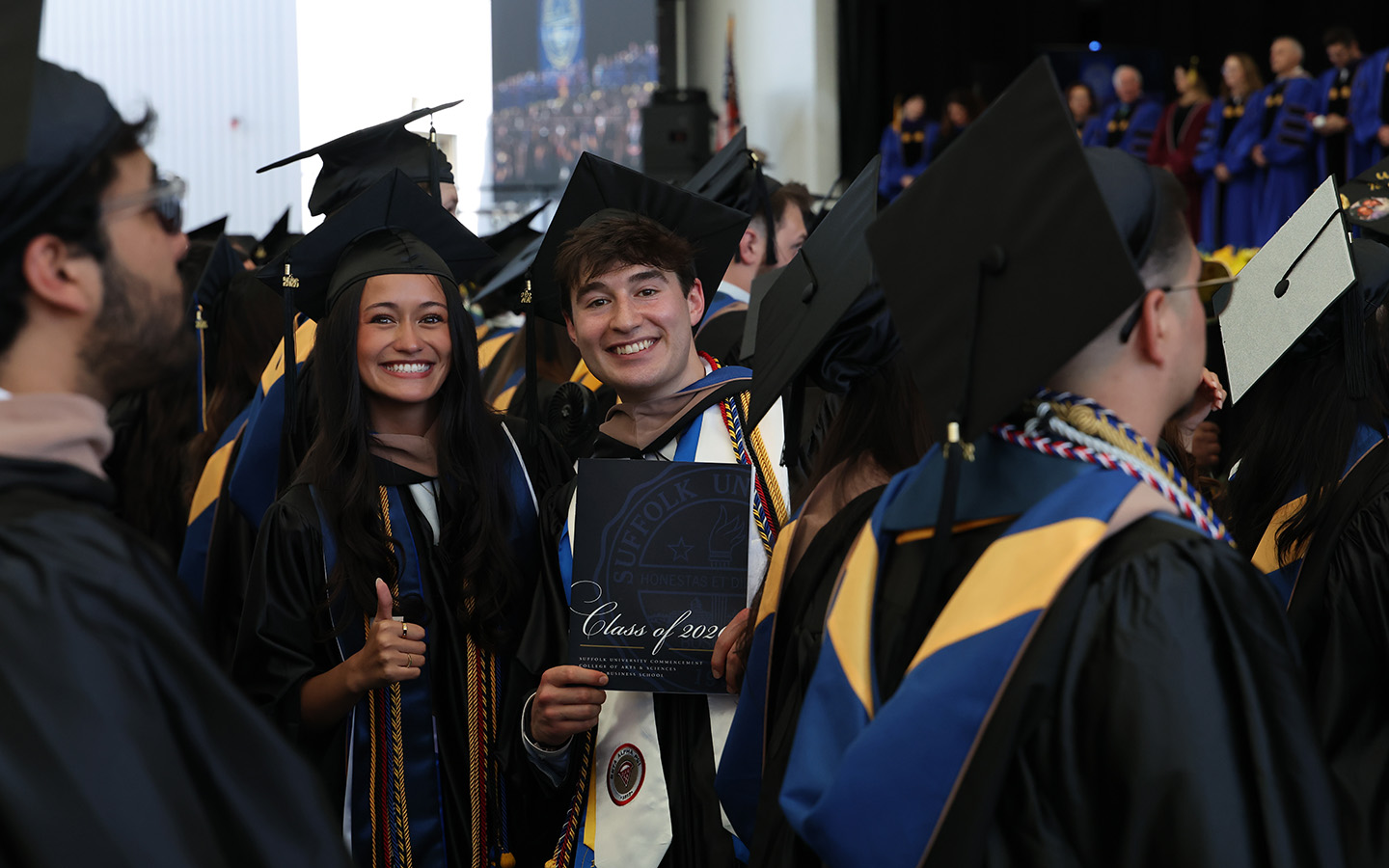 2026 graduates in caps and gowns smile as other graduates process at the 2026 Suffolk University Sawyer Business School Commencement Ceremony.