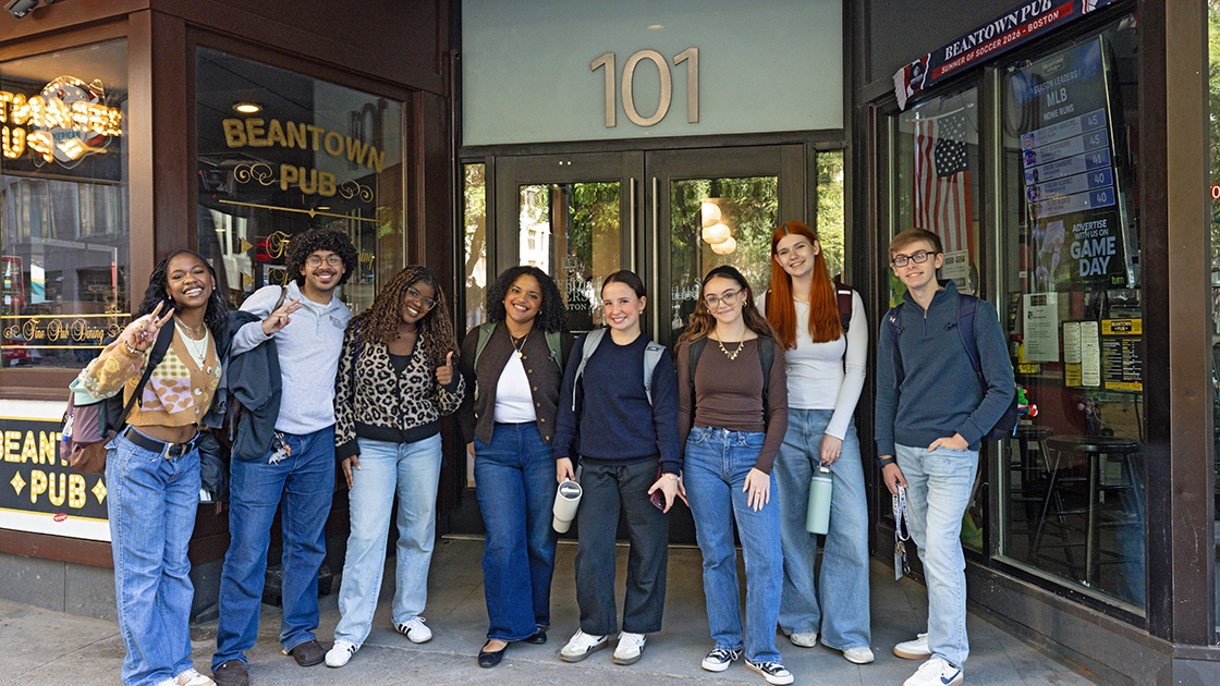 A group of Suffolk students stand together in front of the entry door to 101 Tremont, the newest residence hall on campus.