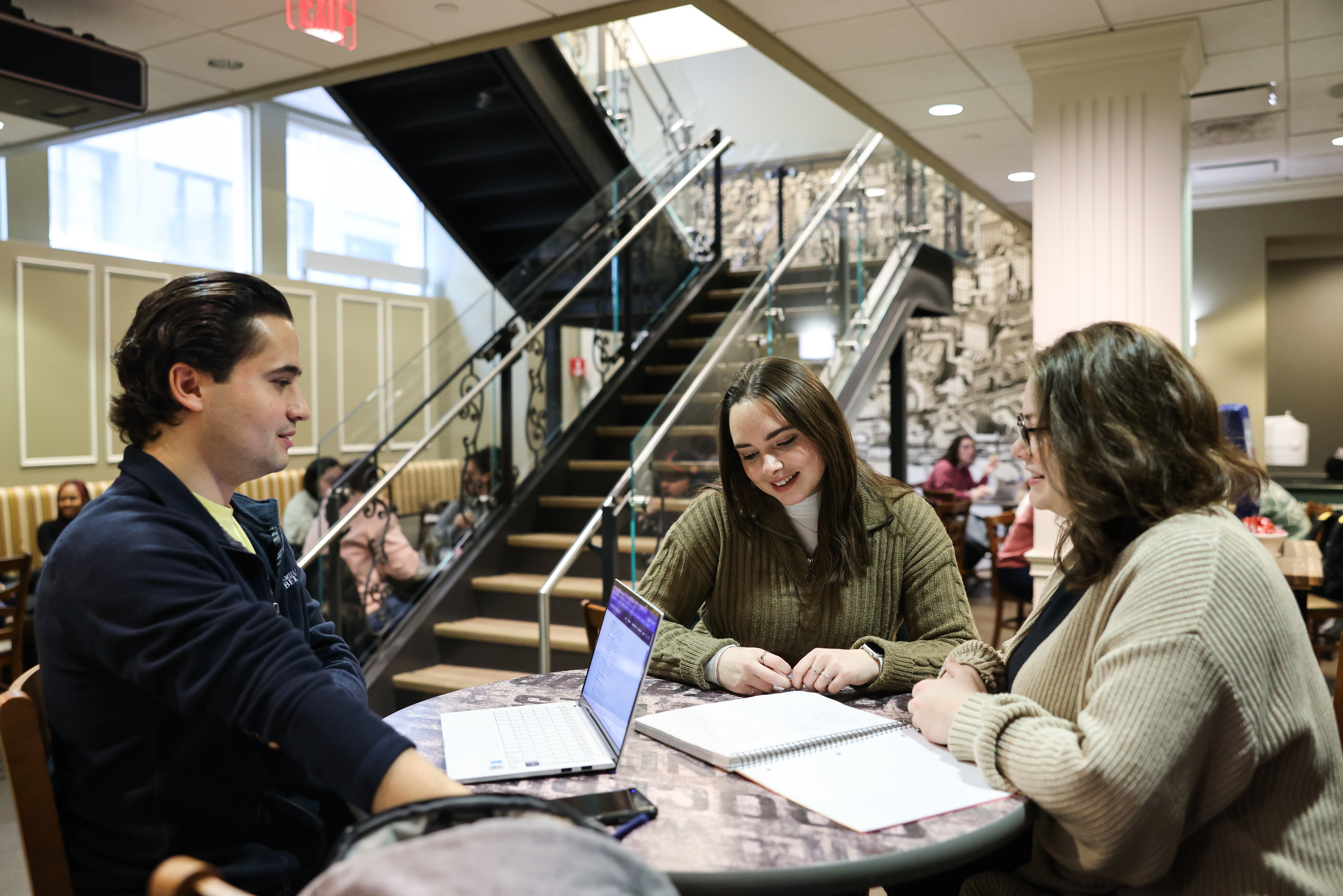 Three students sit together in the library at a table.