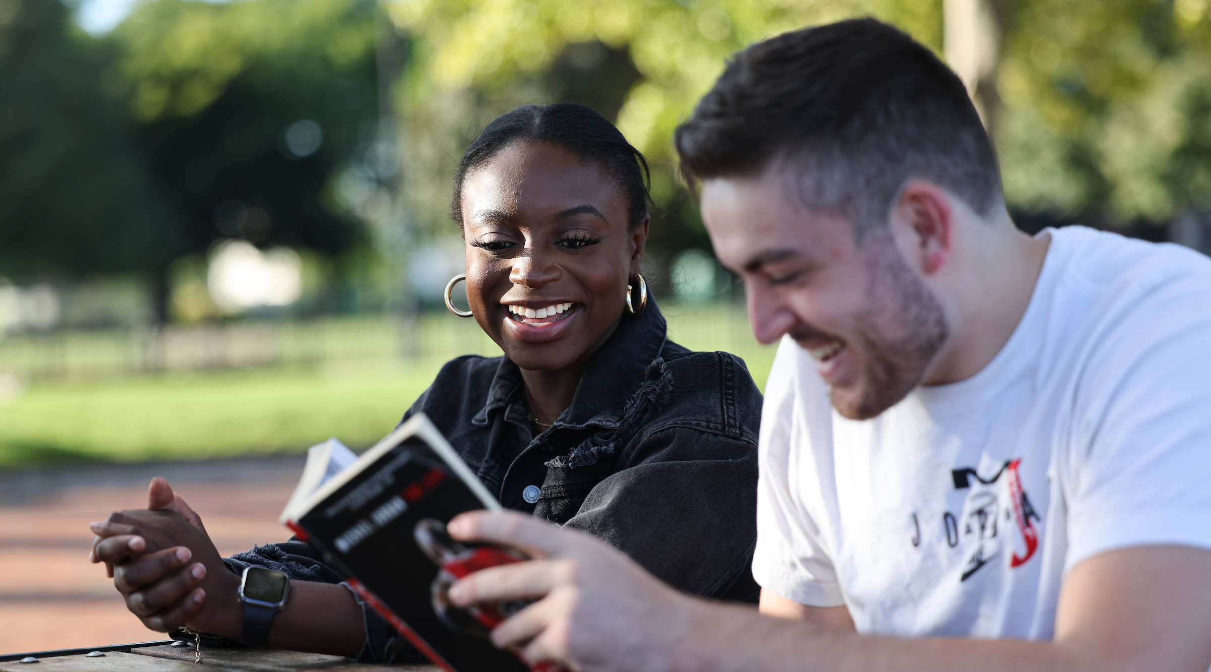 Two Suffolk Students read a book and chat in a city park at a picnic table.